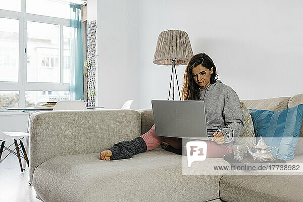 Mature freelancer using laptop sitting on sofa in living room at home