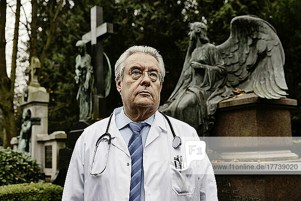 Senior doctor with stethoscope standing on cemetery