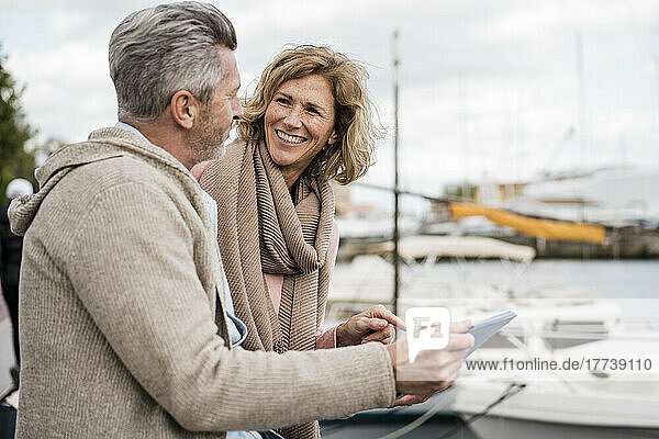 Smiling woman talking with man holding tablet PC at harbor