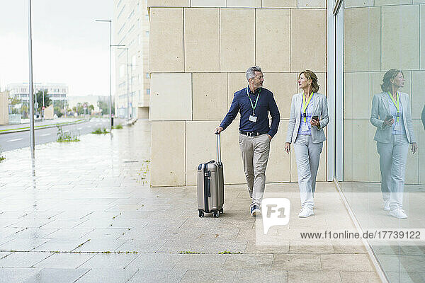 Businessman and businesswoman discussing walking in front of wall