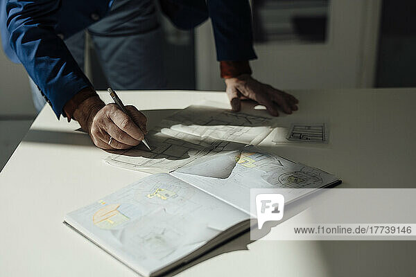 Hands of businessman drawing blueprint at desk in office