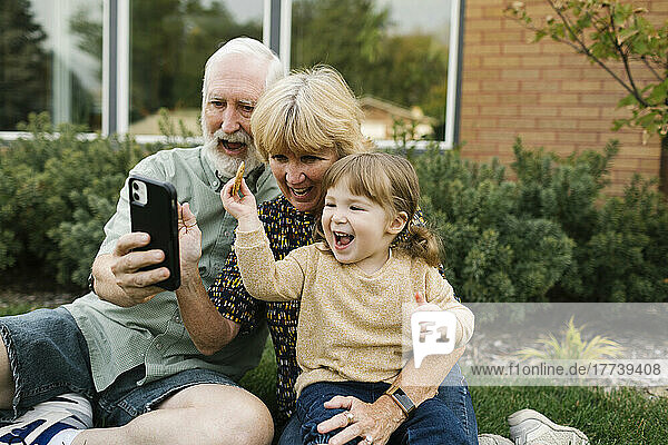 Smiling grandparents taking selfie with granddaughter (4-5) on back yard
