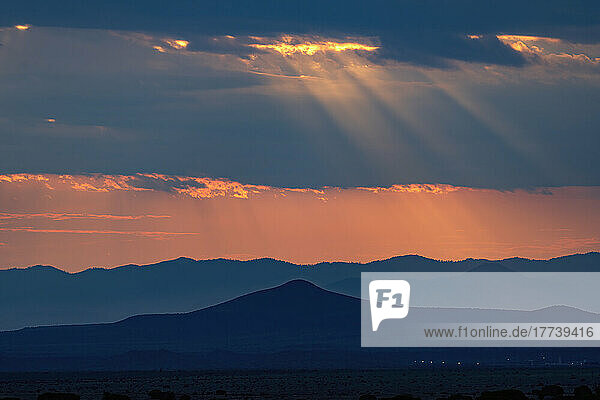 USA  New Mexico  Santa Fe  Sunbeams shining through storm clouds over mountains at sunset 