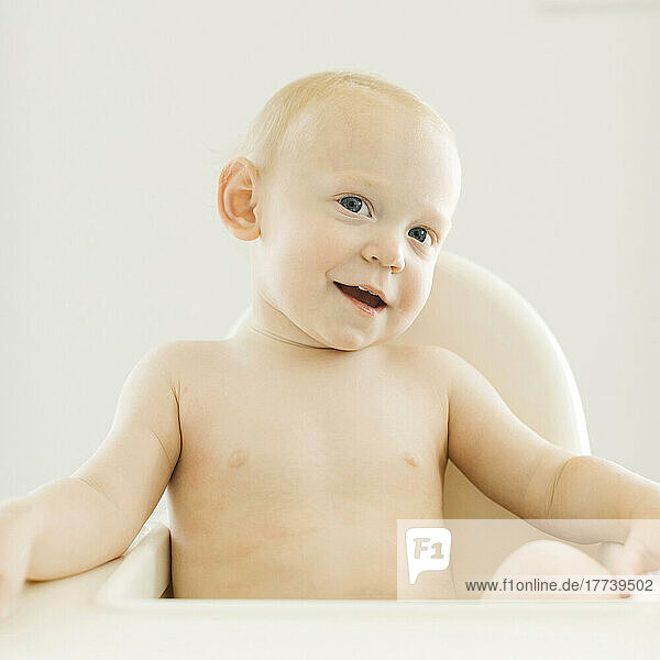Portrait of shirtless baby boy (12-17 months) sitting in high chair