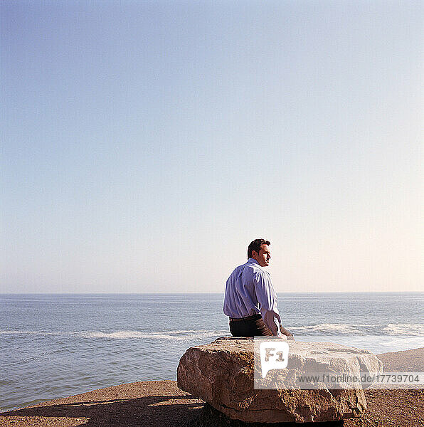 USA  California  Point Mugu  Businessman sitting on rock on beach