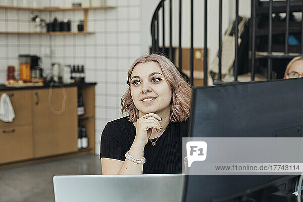 Smiling female entrepreneur with hand on chin at office during meeting