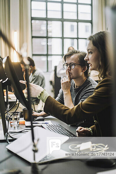 Geschäftsfrau  die auf einen Desktop-PC zeigt  während sie einem männlichen Kollegen im Büro etwas erklärt
