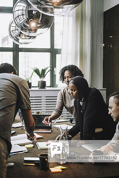 Geschäftsfrauen besprechen einen Plan mit männlichen Kollegen am Konferenztisch in einem kreativen Büro