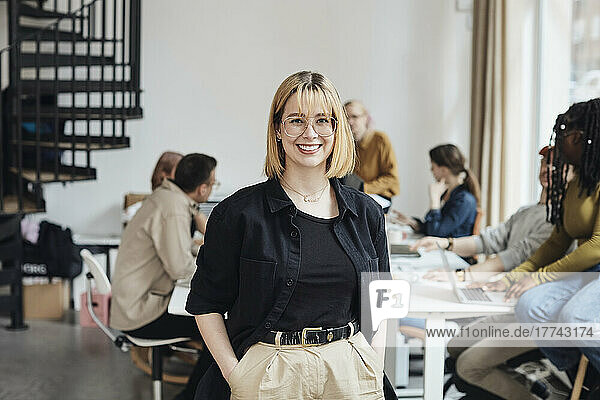 Porträt einer lächelnden jungen Computerprogrammiererin  die mit den Händen in den Taschen in einem Büro eines Start-up-Unternehmens steht