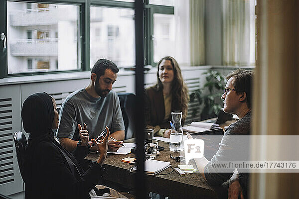 Männliche und weibliche Kollegen hören einer Geschäftsfrau zu  die am Konferenztisch sitzend Ideen diskutiert