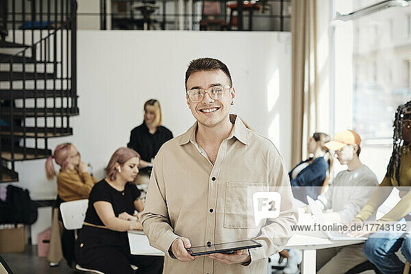Portrait of smiling male programmer holding tablet PC while standing in office