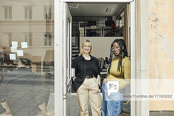 Portrait of young female entrepreneurs with hands in pockets standing at office doorway