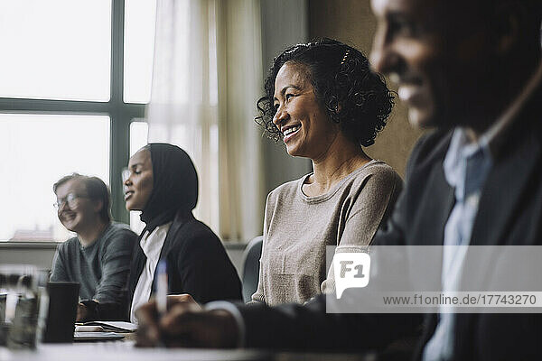 Lächelnde reife Geschäftsfrau sitzt mit männlichen und weiblichen Kollegen in einem Besprechungsraum