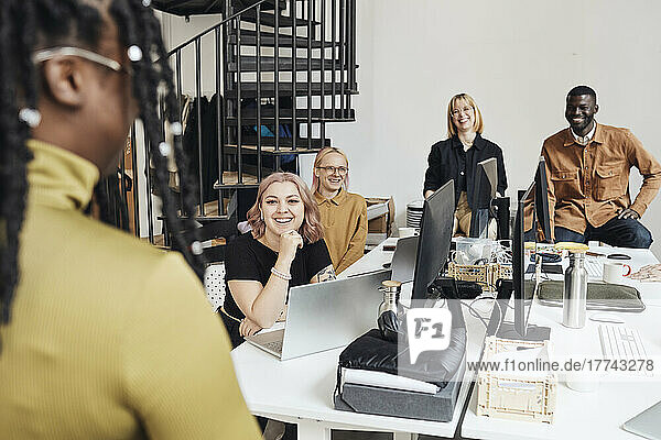 Lächelnde Kollegen  die eine Geschäftsfrau während einer Besprechung im Büro ansehen