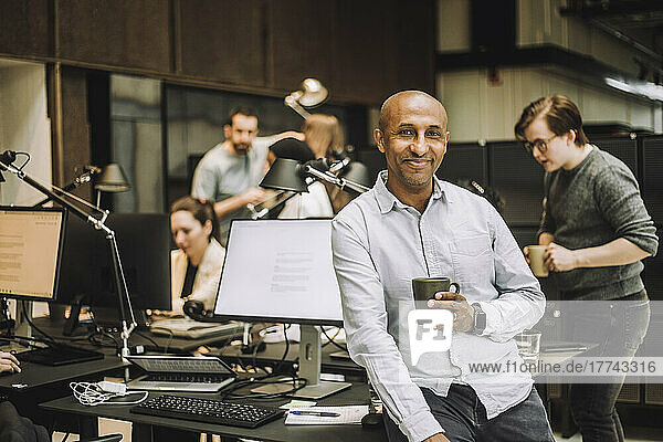 Portrait of smiling bald businessman with coffee mug sitting on desk in office