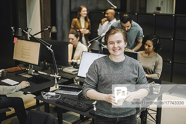 Porträt eines lächelnden jungen Geschäftsmannes mit Kaffeetasse auf dem Schreibtisch im Büro