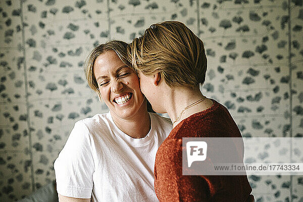 Woman embracing happy girlfriend against wall at home