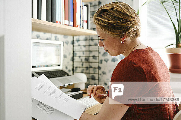 Businesswoman examining documents at desk during work from home