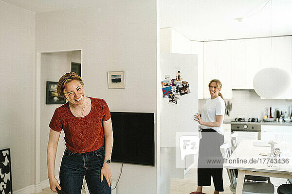 Woman laughing while girlfriend standing in kitchen at home
