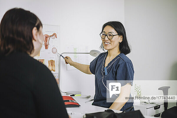 Glücklicher reifer Arzt  der einem Patienten die Organe erklärt  während er auf eine Tabelle in einer medizinischen Klinik zeigt