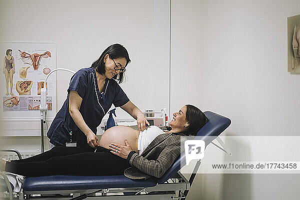 Lächelnde Ärztin misst den Bauch einer schwangeren Frau bei einer Untersuchung in einer medizinischen Klinik