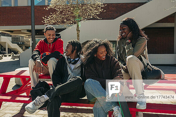 Glückliche multirassische junge Freunde unterhalten sich auf einer Bank sitzend