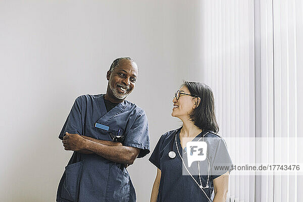 Happy healthcare experts looking at each other against white wall in hospital