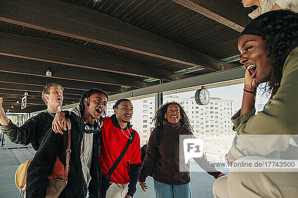 Playful multiracial young friends singing at railroad station platform