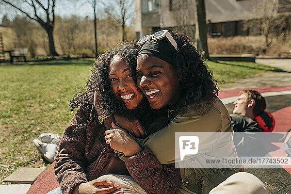 Happy multiracial female friends embracing each other while sitting in playground on sunny day