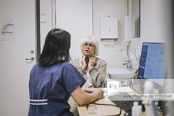 Ältere Frau erklärt einem HNO-Arzt  der am Schreibtisch in einer medizinischen Klinik sitzt  ihr Halsproblem