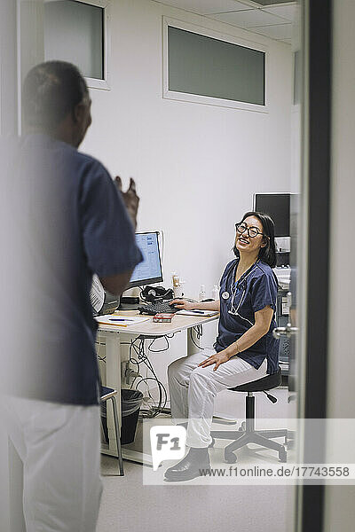 Lächelnde Ärztin im Gespräch mit einem männlichen Kollegen  der an der Tür einer medizinischen Klinik steht