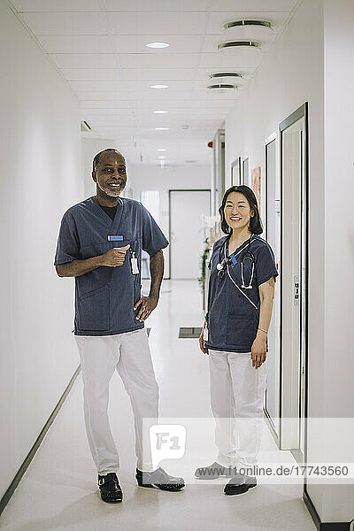 Full length portrait of smiling male and female healthcare worker standing in corridor at medical clinic