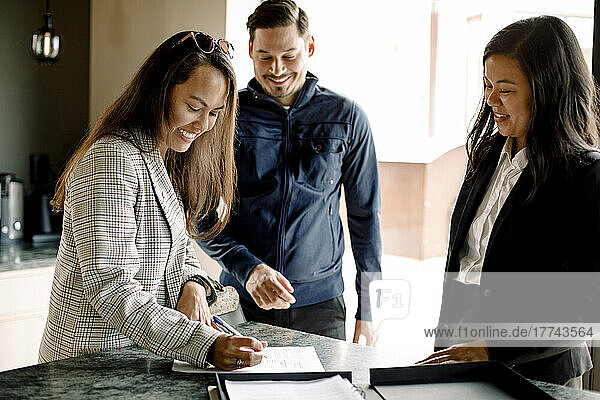 Ehepaar bei der Vertragsunterzeichnung mit einem Immobilienmakler an der Kücheninsel des neuen Hauses