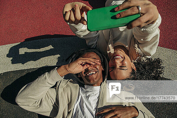 Glückliche junge Freunde nehmen Selfie durch Smartphone  während in Spielplatz liegen