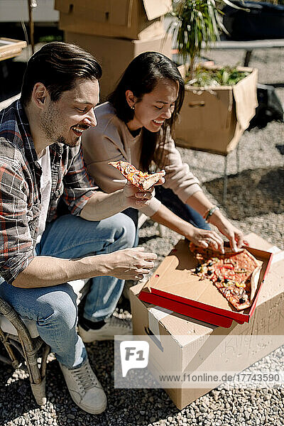 Smiling couple eating pizza while relocating in new house