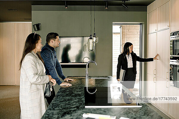 Immobilienmakler zeigt einem Paar die Küchenschränke des neuen Hauses