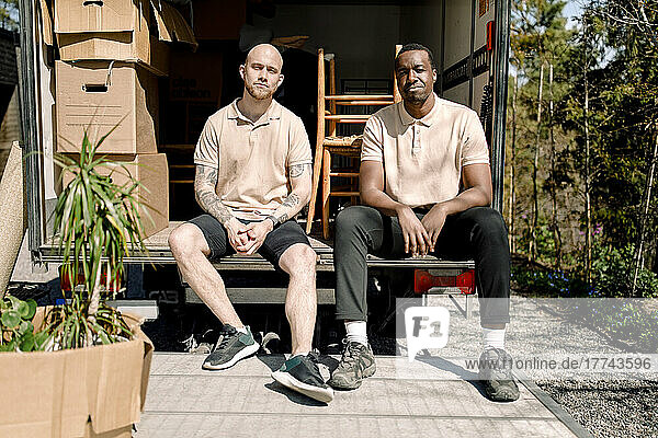 Porträt von multirassischen Umzugshelfern  die am Kofferraum eines Lieferwagens sitzen