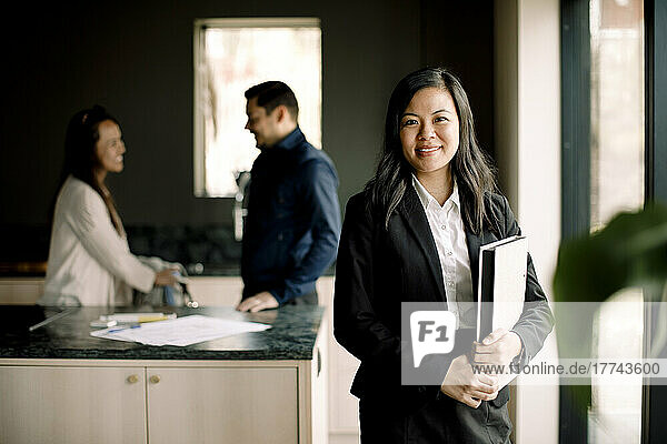 Porträt eines lächelnden Immobilienmaklers mit einem Paar im Hintergrund in einem neuen Haus