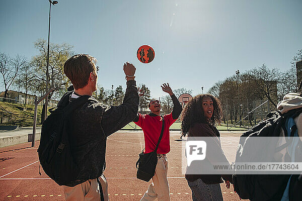 Men playing with ball while walking with friends in sports court on sunny day