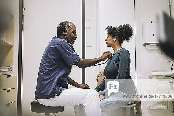 Male healthcare worker with stethoscope examining female patient in hospital