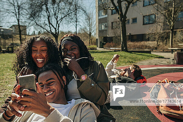 Glückliche junge Freunde teilen Smartphone zusammen auf dem Spielplatz an einem sonnigen Tag