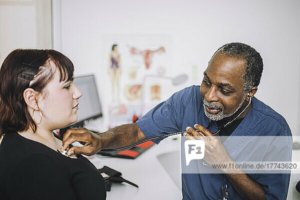 Männlicher Gesundheitsexperte mit Stethoskop bei der Untersuchung einer Patientin in einer Klinik