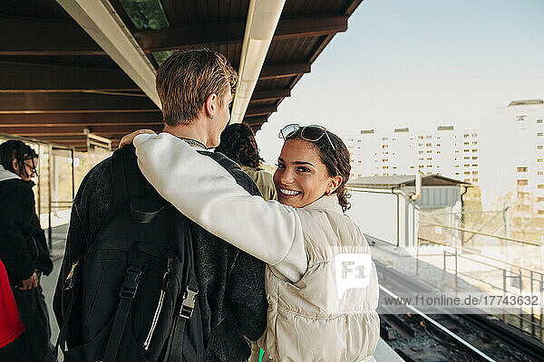 Porträt einer lächelnden Frau  die den Arm um einen Freund legt  der auf einem Bahnhof spazieren geht