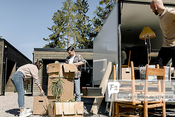 Ehepaar öffnet Kartons  während ein Lieferant Möbel vom Lastwagen ablädt