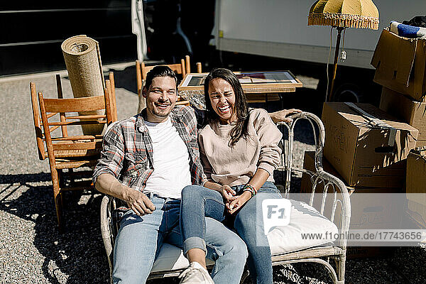 Portrait of smiling couple sitting on chair during sunny day