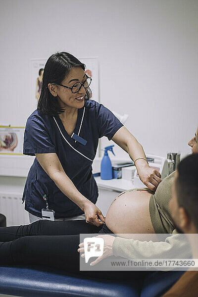 Smiling female doctor measuring abdomen of pregnant woman in medical clinic