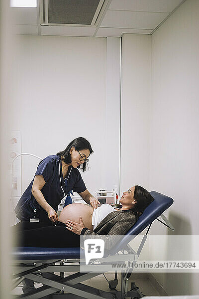 Female healthcare expert measuring abdomen of pregnant woman lying on gurney in medical clinic