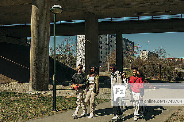 Multiracial male and female friends walking together on road during sunny day