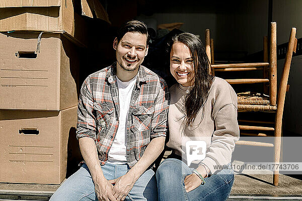 Portrait of smiling couple sitting in back of delivery truck