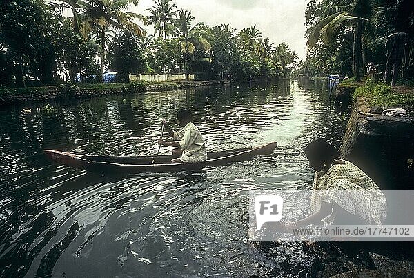 Ein Mann fährt mit dem Kajak auf den Backwaters und eine Frau badet ihr Kind am Ufer des Backwater in Kodungallur  Kerala  Indien  Asien
